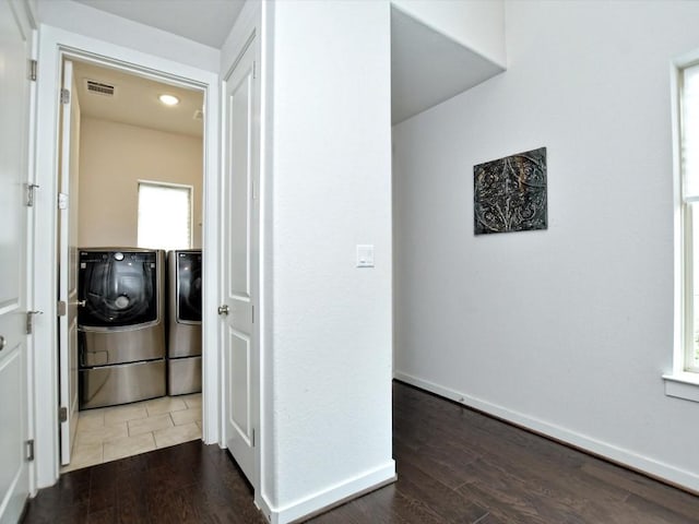 hallway with dark wood-style flooring, washer and clothes dryer, visible vents, and baseboards