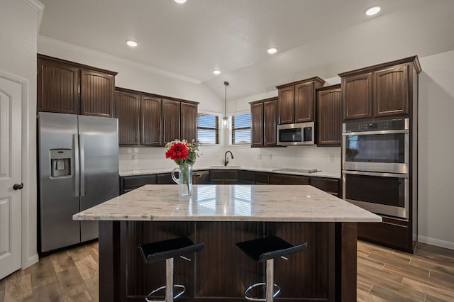 kitchen with appliances with stainless steel finishes, a center island, dark brown cabinets, and wood finished floors