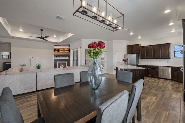 dining space with ceiling fan, dark wood-type flooring, visible vents, ornamental molding, and a raised ceiling