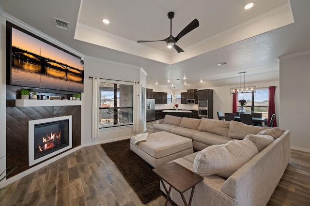 living room featuring dark wood-style floors, a glass covered fireplace, a raised ceiling, and visible vents