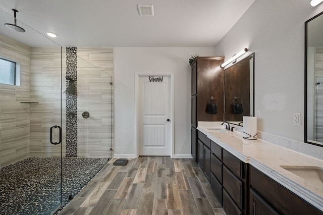 full bath featuring wood finish floors, double vanity, visible vents, a stall shower, and baseboards