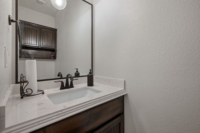 bathroom with a textured wall, visible vents, and vanity