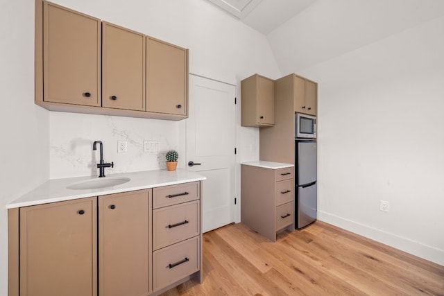 kitchen with lofted ceiling, stainless steel appliances, a sink, light wood-style floors, and light countertops