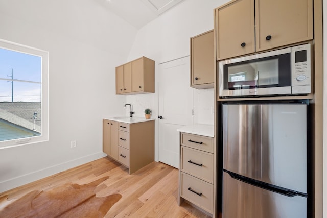 kitchen with a sink, baseboards, light wood-style floors, light countertops, and appliances with stainless steel finishes