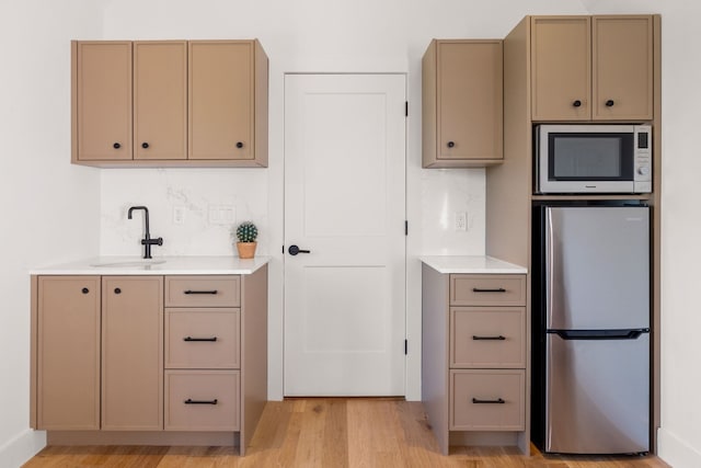 kitchen with a sink, stainless steel appliances, light wood finished floors, and light countertops