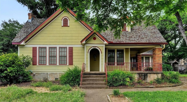 view of front of house with a porch, roof with shingles, brick siding, and a chimney