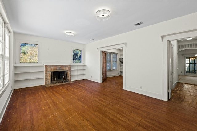 unfurnished living room featuring a wealth of natural light, a brick fireplace, and dark wood finished floors