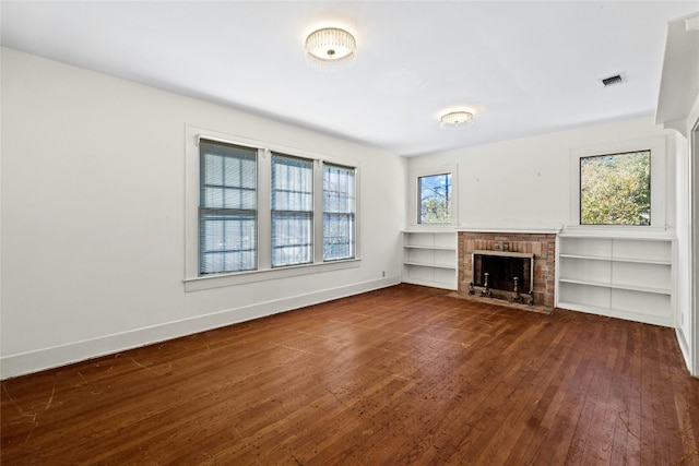 unfurnished living room featuring a brick fireplace, dark wood finished floors, visible vents, and baseboards