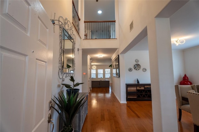 foyer featuring crown molding, visible vents, a high ceiling, wood finished floors, and baseboards