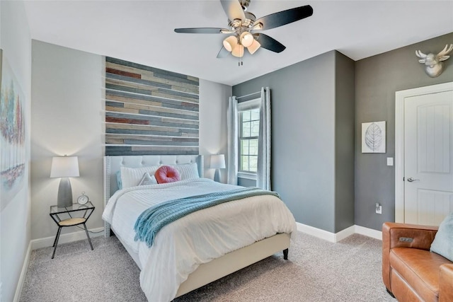 bedroom with ceiling fan, an accent wall, baseboards, and light colored carpet