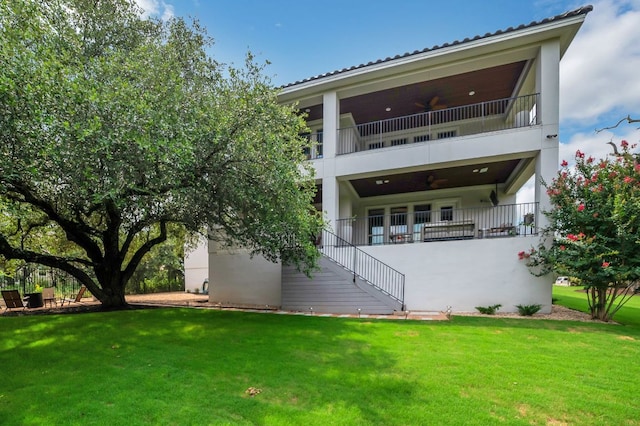 back of house featuring ceiling fan, stairs, a lawn, and stucco siding