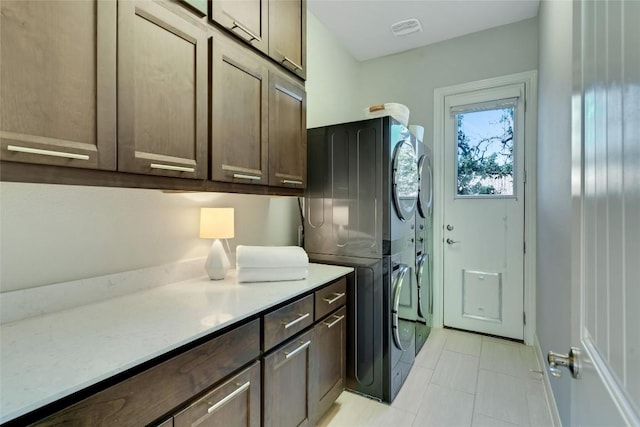 washroom with visible vents, cabinet space, and stacked washer / drying machine