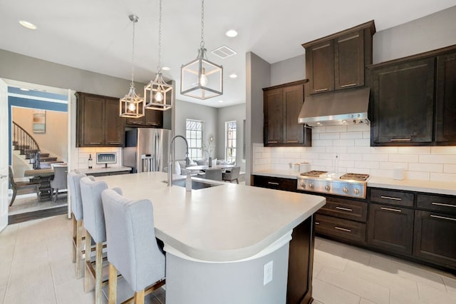 kitchen featuring stainless steel appliances, visible vents, light countertops, range hood, and a center island with sink