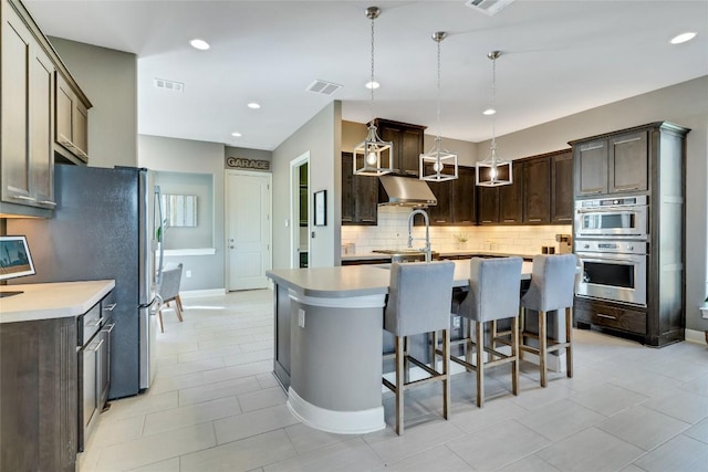 kitchen with an island with sink, decorative light fixtures, light countertops, dark brown cabinets, and under cabinet range hood