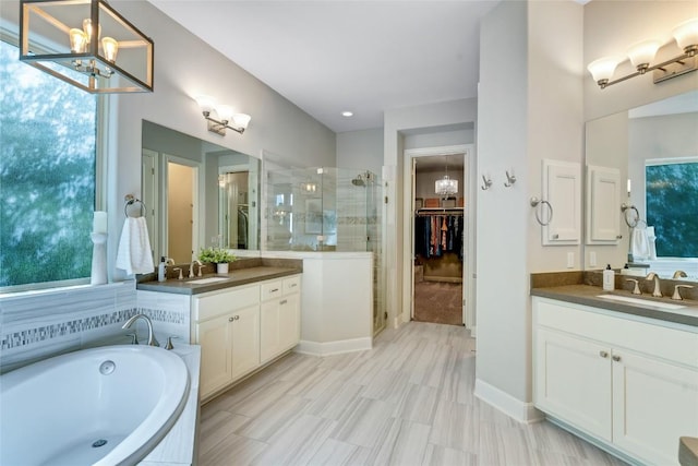 bathroom featuring a stall shower, two vanities, a sink, a spacious closet, and a notable chandelier