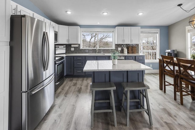 911 Sandy Mountain Dr, Sunrise Beach, TX 78643 - kitchen with stainless steel appliances, a sink, backsplash, light wood finished floors, and a breakfast bar