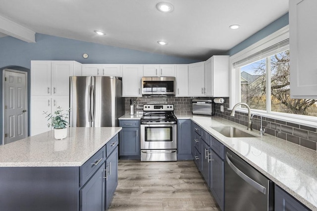 kitchen featuring blue cabinets, a sink, white cabinetry, vaulted ceiling, and appliances with stainless steel finishes