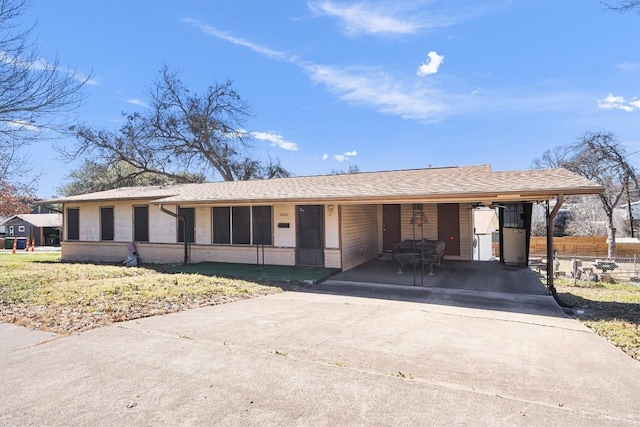 ranch-style home featuring roof with shingles, an attached carport, concrete driveway, and brick siding