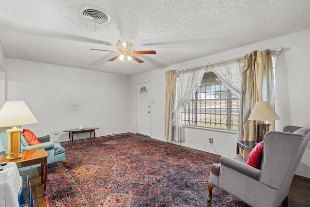 living area with visible vents, ceiling fan, a textured ceiling, and heating unit