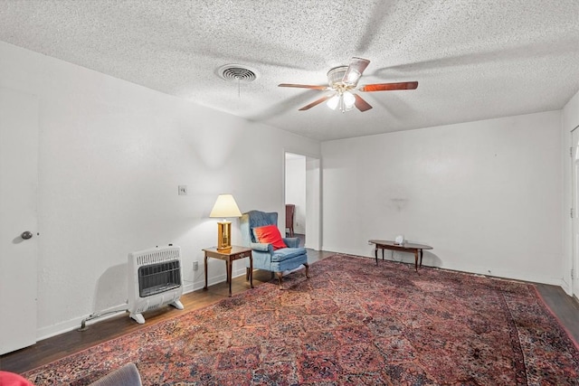 living area with ceiling fan, dark wood-style flooring, visible vents, and heating unit