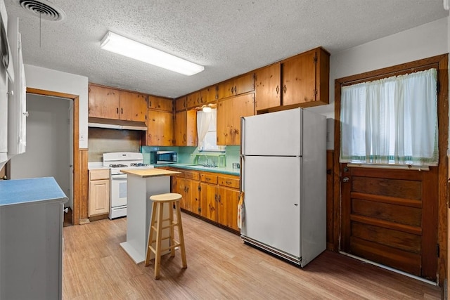 kitchen featuring light countertops, white appliances, under cabinet range hood, and brown cabinets