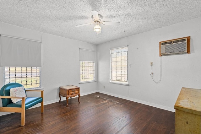 sitting room featuring baseboards, a wall unit AC, dark wood-style floors, ceiling fan, and a textured ceiling