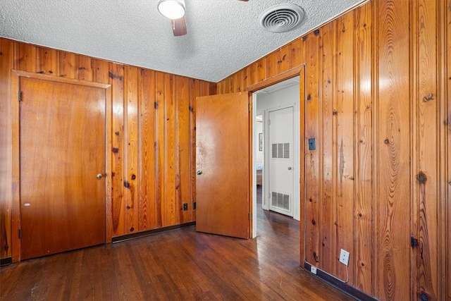 unfurnished bedroom with dark wood-style flooring, visible vents, and wood walls