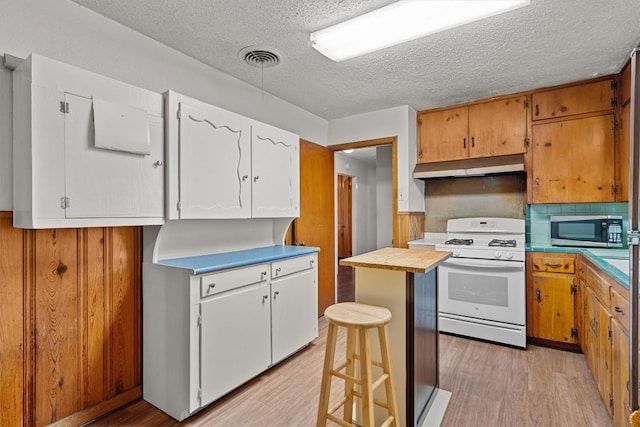 kitchen featuring white gas range, stainless steel microwave, white cabinets, and light countertops