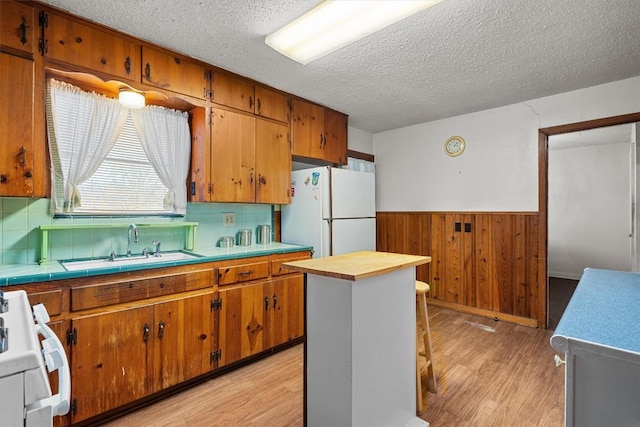 kitchen featuring a kitchen island, light countertops, range, freestanding refrigerator, and brown cabinetry