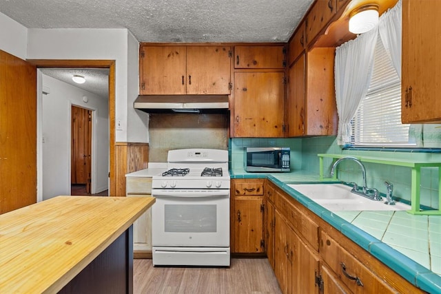 kitchen with stainless steel microwave, white gas range, light countertops, under cabinet range hood, and a sink