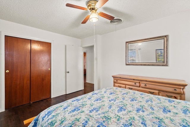 bedroom with dark wood-style floors, a closet, visible vents, a ceiling fan, and a textured ceiling