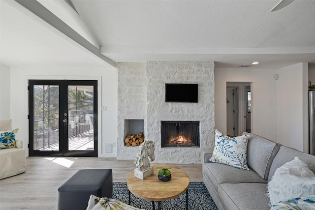 living room featuring a stone fireplace, french doors, and light wood-style flooring