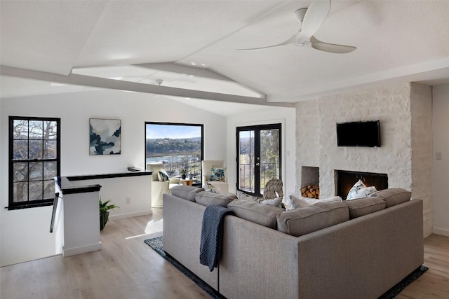 living area with lofted ceiling, a large fireplace, light wood-type flooring, and baseboards