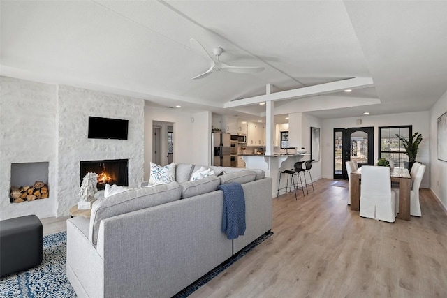 living area with baseboards, ceiling fan, vaulted ceiling, light wood-style floors, and a fireplace