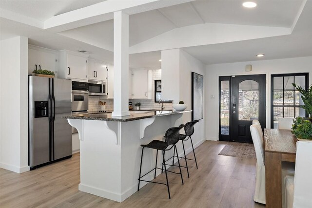 1201 Lake Shore Dr, Spicewood, TX 78669 - kitchen featuring stainless steel appliances, lofted ceiling, white cabinets, a kitchen bar, and tasteful backsplash
