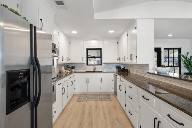 kitchen with stainless steel appliances, a sink, white cabinets, decorative backsplash, and dark stone countertops