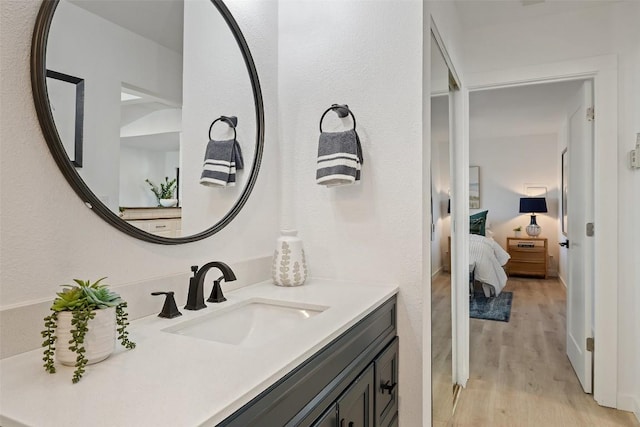 ensuite bathroom with connected bathroom, vanity, and wood finished floors