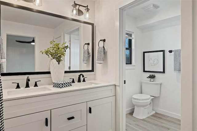 full bath with double vanity, wood finished floors, a sink, and toilet