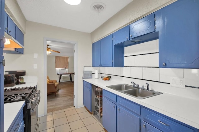 kitchen with a sink, light countertops, blue cabinetry, stainless steel gas range, and backsplash