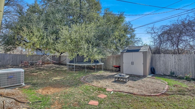 view of yard featuring a storage shed, a fenced backyard, an outbuilding, a trampoline, and cooling unit