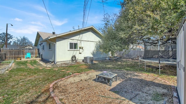 rear view of house featuring a trampoline, an outdoor fire pit, a fenced backyard, and stucco siding