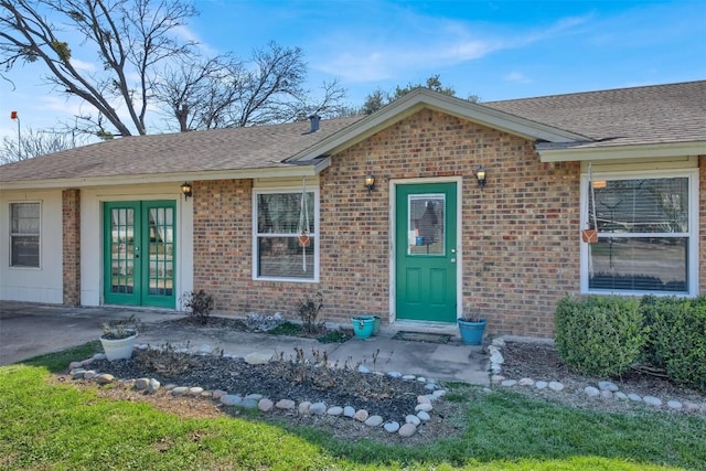 doorway to property featuring brick siding, roof with shingles, and french doors