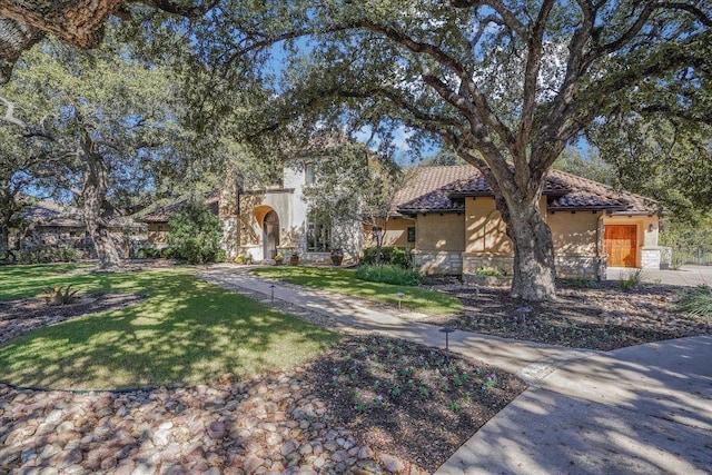 mediterranean / spanish-style home featuring a front yard, stone siding, a tile roof, and stucco siding