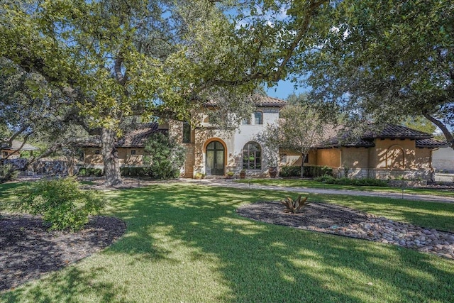 view of front facade with stone siding, a tile roof, a front lawn, and stucco siding