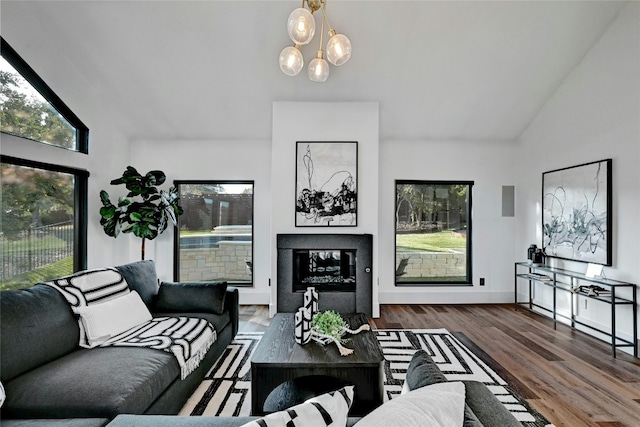 living room with a chandelier, baseboards, vaulted ceiling, dark wood-style floors, and a glass covered fireplace