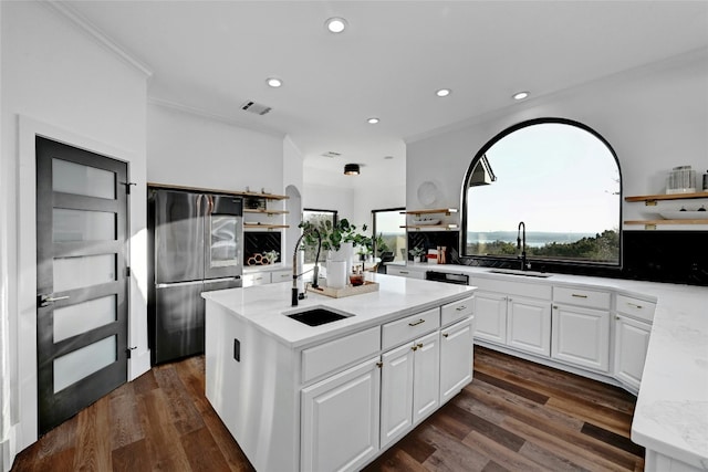 kitchen with white cabinets, a kitchen island, stainless steel refrigerator, light stone countertops, and a sink