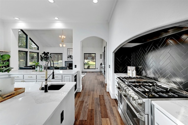 kitchen with tasteful backsplash, hanging light fixtures, white cabinetry, a sink, and double oven range