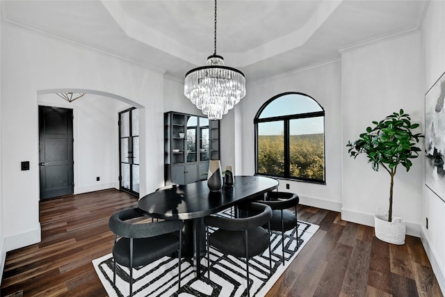 dining space featuring baseboards, arched walkways, dark wood-type flooring, and a tray ceiling