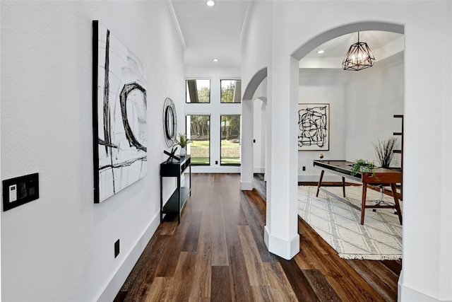 hall with baseboards, arched walkways, dark wood finished floors, and crown molding