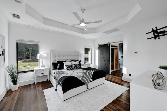 bedroom featuring dark wood-type flooring, a tray ceiling, a barn door, and visible vents